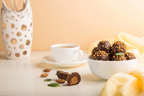 Chocolate caramel ball candies with almonds and a cup of coffee on a white and orange background