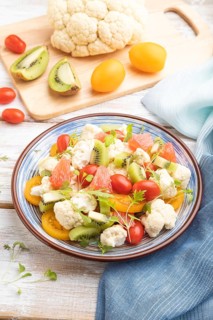 Vegetarian salad of cauliflower cabbage, kiwi, tomatoes, microgreen sprouts on white wooden