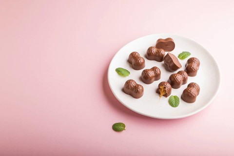 Chocolate caramel candies on a pastel pink background. Side view, copy space, close up