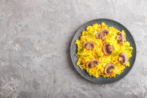 Yellow fried rice with champignons mushrooms, turmeric and oregano on blue ceramic plate on a gray