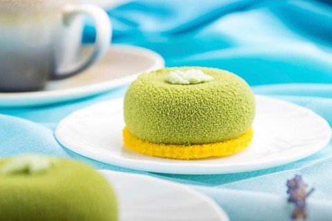 Green mousse cake with pistachio cream and a cup of coffee on a white wooden background and blue