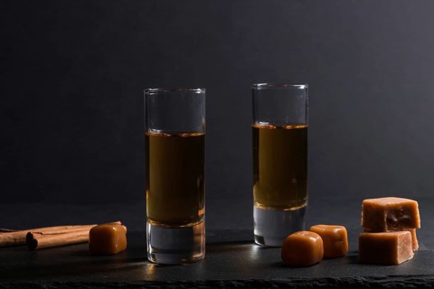 Glass of whiskey with caramel candies on a black stone slate board on black background. Side view,