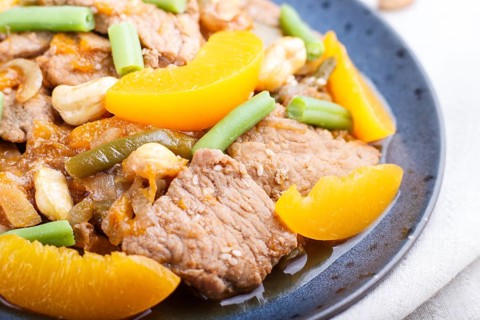 Fried pork with peaches, cashew and green beans on a black concrete background. Side view, close