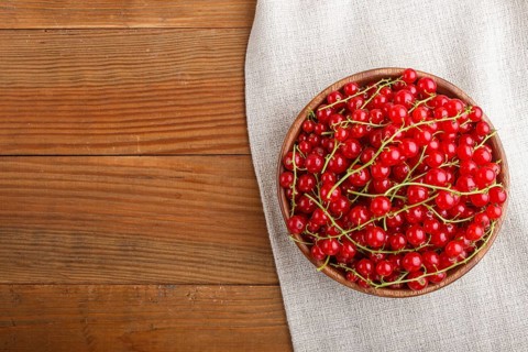 Fresh red currant in wooden bowl on wooden background. top view, flat lay, copy space