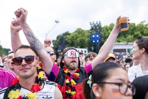 A fan celebrates with sunglasses, beer and feather boa in the fan zone at the Brandenburg Tor