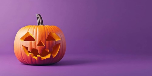 Halloween banner with orange carved pumpkin lantern on purple background with copy space.