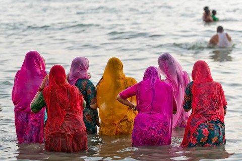 Hindu pilgrims, woman in colourful saris, take a holy dip in the sea in front of sunrise at Ghat