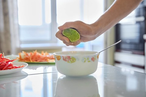 A hand squeezes a lime over a white bowl, adding fresh juice to enhance flavors while chopping