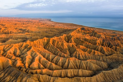 Landscape of eroded hills, badlands at sunset, Lake Issyk Kul in the background, aerial view,