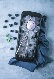 Blueberry ice cream, container with a spoon, on a gray table, fresh blueberries