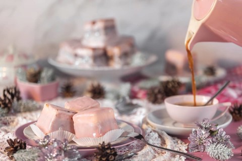 Coffee is poured into a pink cup, alongside cake, punch doughnuts and Christmas decorations