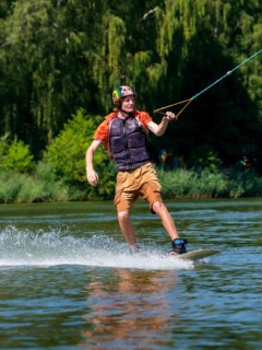 Young casual man with flapping shirt on wakeboard in lake, water ski and wakepark, Stráž pod