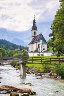 Parish church of St Sebastian by a river in an idyllic Alpine landscape with mountains and forests