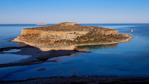 Island surrounded by calm sea with rocky cliffs, under clear day skies, natural beauty, Gramvoussa,