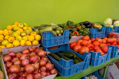 Market stall with various vegetables such as tomatoes, onions, peppers and lemons in blue boxes in