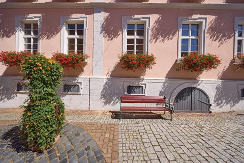 Facade of a house with windows and flower boxes with blooming geraniums, bench, planter with a