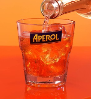 Aperol on ice cube cubes in an aperitif tumbler against an orange background is topped up with soda