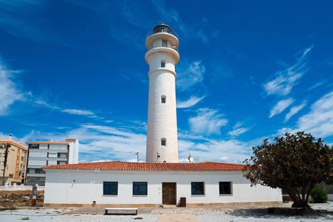 White lighthouse with neighbouring building under blue sky with clouds, sunny atmosphere, Faro de