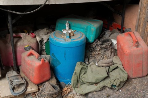 Old and dusty empty red plastic gas canisters, blue water containers and boots stored underneath a