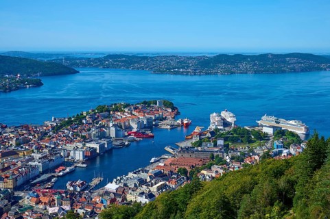 Panoramic view of a coastal town with harbour and a variety of buildings, surrounded by mountains