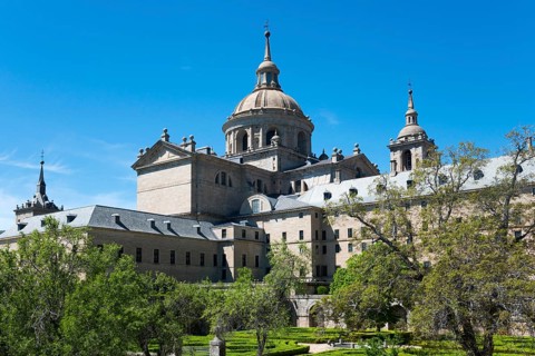 Impressive historic monastery with towers and domes surrounded by green trees under a blue sky,
