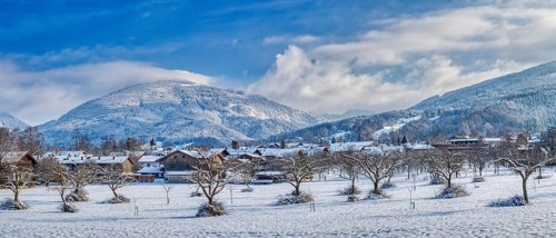 Snow-covered landscape with trees and village, in the background mountains under a blue sky, Bad