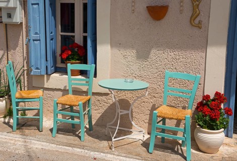 Cosy Mediterranean outdoor area with green chairs and blue shutters in front of a beige wall with