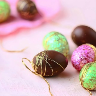 Small chocolate Easter eggs wrapped in shiny foil, placed on a bed of shredded pastel-colored