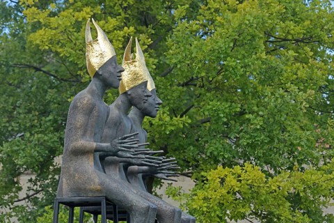 Sculpture Enthroned by Volkmar Kühn 2021, three bishops with golden mitres sitting on stool, row,