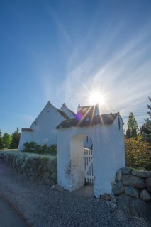 Whitewashed church in Dalby, backlight, stone wall made of boulders, entrance gate, Fyn, North