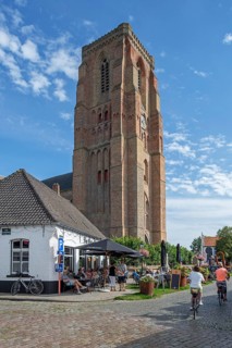 Tourists at sidewalk café and 13th century Gothic bell tower of Our Lady's Church in the village