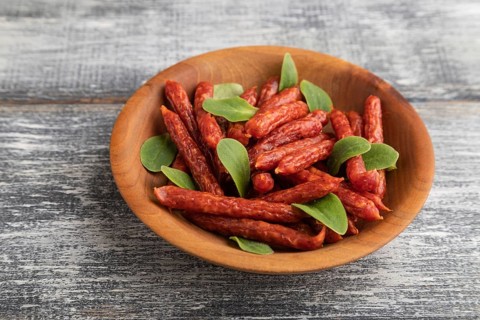Small smoked sausage with borage microgreen, salt and pepper on gray wooden background. Side view,