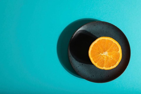 Ripe cut orange on blue ceramic plate on blue pastel background. Top view, flat lay, copy space,