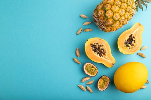 Ripe cut papaya, pineapple, melon, passion fruit, almonds on blue pastel background. Top view, flat