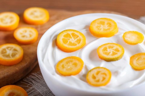 Greek yogurt with kumquat pieces in a white plate on a brown wooden background, close up
