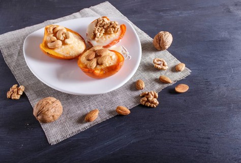 Persimmon dessert with curd, nuts and milk cream on black wooden background. close up, copy space