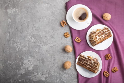 Homemade cake with milk cream and walnuts with cup of coffee on a gray concrete background and