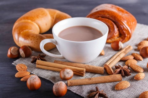 A cup of hot chocolate with nuts, buns and spices on linen napkin and black wooden background.