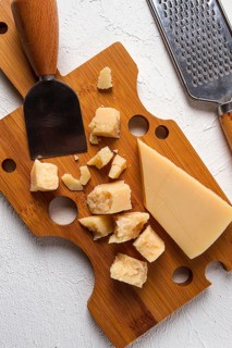 Hard cheese, parmesan, on a cutting board, cheese knife, grater, top view, no people