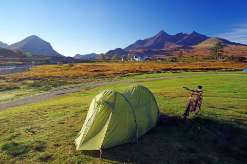 A tent and a bicycle stand on a green meadow with mountains in the background, ideal for camping,