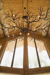 Illuminated deer antlers chandelier hanging from high cathedral knotty pine wood planks ceiling