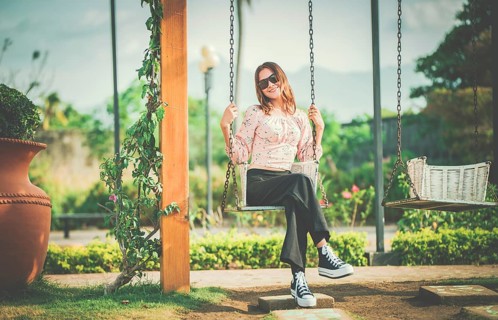 Happy young woman sitting on a swing in a nature park. Portrait of a smiling girl sitting on a