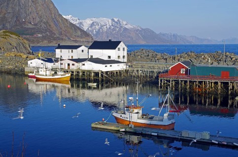 Small harbour with boats, white houses and surrounding mountains reflected in the calm water under