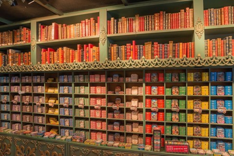 Wall of shelves with books on top and numerous colourful tins underneath, tins of sardines, tinned