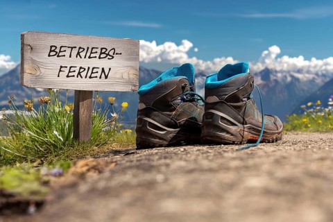 Symbolic image of company holidays/summer holidays: Hiking boots in front of an alpine backdrop and
