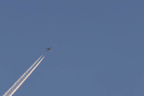 Boeing 787-8 Dreamliner aircraft flying across a blue sky with a vapour trail or contrail behind,