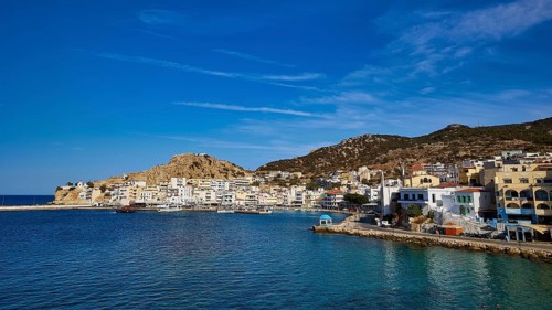 An idyllic coastal town with white buildings and hills, surrounded by blue water under a clear sky,
