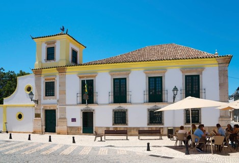 Colonial-style building with yellow accents, outdoor seating under parasols, Consulado-Geral do