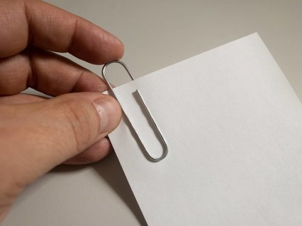 A hand attaches a paper clip to a piece of white paper