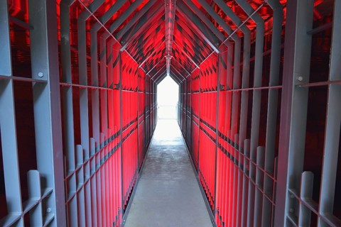 A long tunnel with red lighting and metallic structures conveys a futuristic and industrial
